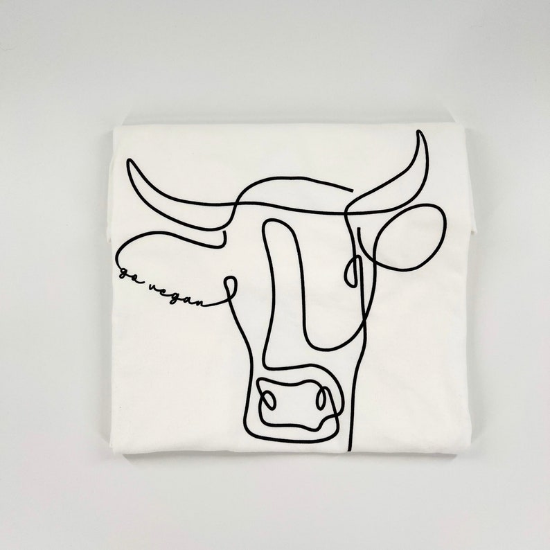 May include: White t-shirt with a black line drawing of a cow's head and the text "go vegan" underneath.