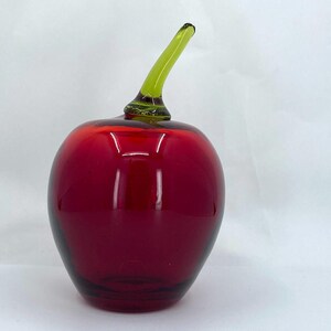 May include: A red glass apple with a green glass stem. The apple is a decorative object.