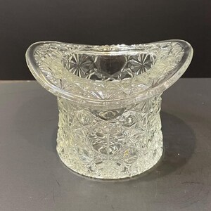 May include: A clear glass hat-shaped dish with a cut-glass design. The dish is perfect for holding small items like jewelry or candy.