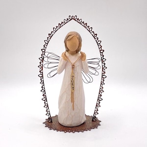 May include: A white porcelain angel figurine with a gold necklace and a tag that reads "2011". The angel is standing on a brown metal base with a decorative design.