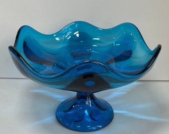 Könnte beinhalten: Eine blaue Glasschüssel mit gewelltem Rand und einem Sockel. Die Schüssel ist aus klarem Glas mit einer blauen Tönung.