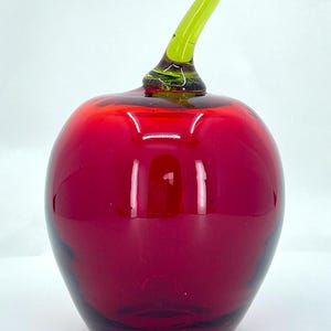 May include: A red glass apple with a green glass stem. The apple is a decorative object.