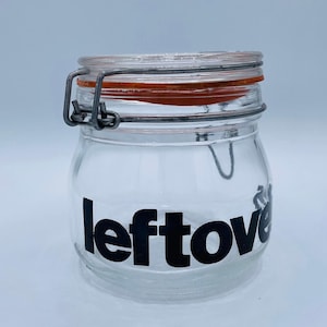 Op de afbeelding: Een glazen pot met een metalen sluiting en een zwart etiket met de tekst "restjes".