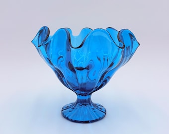 Könnte beinhalten: Eine blaue Glasschüssel mit gewelltem Rand und einem Sockel. Die Schüssel ist aus klarem Glas mit einer blauen Tönung.