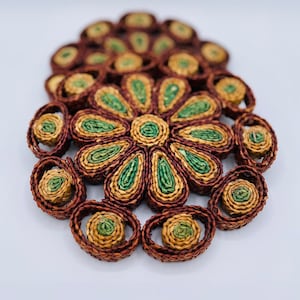 May include: Set of two woven brown and green floral-shaped trivets. The trivets are made of natural materials and have a rustic look.