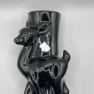 Könnte beinhalten: Schwarze Keramikvase in Form eines Hirsches, der auf einem Baumstumpf steht. Die Vase hat eine glänzende Oberfläche.