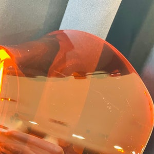 Pu&ograve; includere: Primo piano di una bottiglia di plastica trasparente colorata di arancione con una superficie testurizzata.
