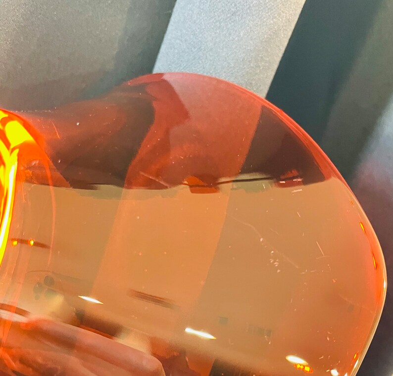 Pu&ograve; includere: Primo piano di una bottiglia di plastica trasparente colorata di arancione con una superficie testurizzata.