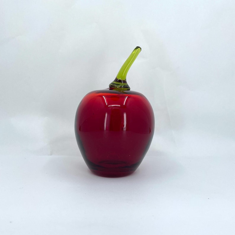 May include: A red glass apple with a green glass stem. The apple is a decorative object.