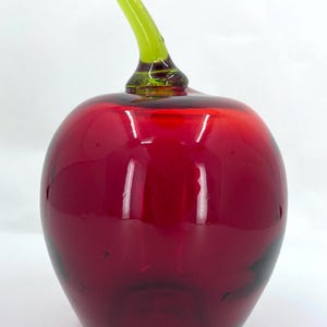 May include: A red glass apple with a green glass stem. The apple is a decorative object.
