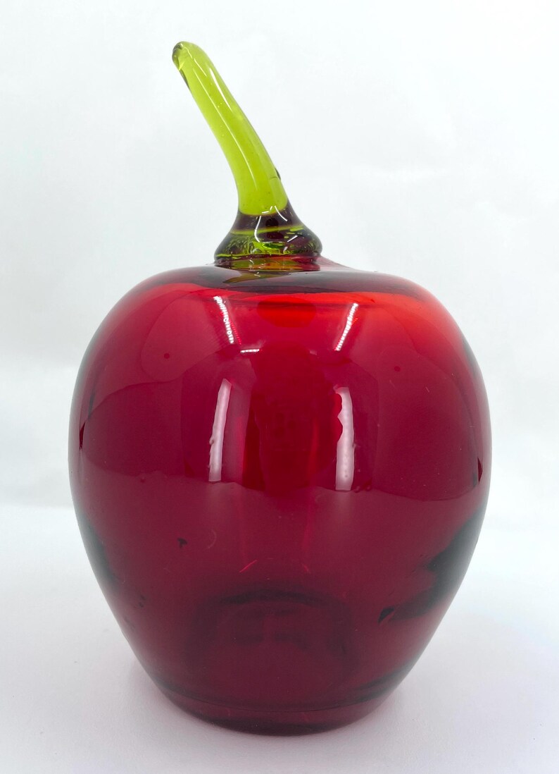 May include: A red glass apple with a green glass stem. The apple is a decorative object.