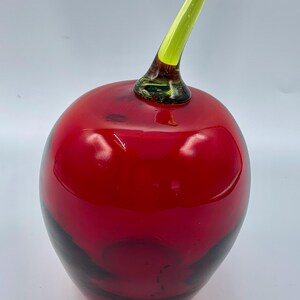 May include: A red glass apple with a green glass stem. The apple is a decorative object.
