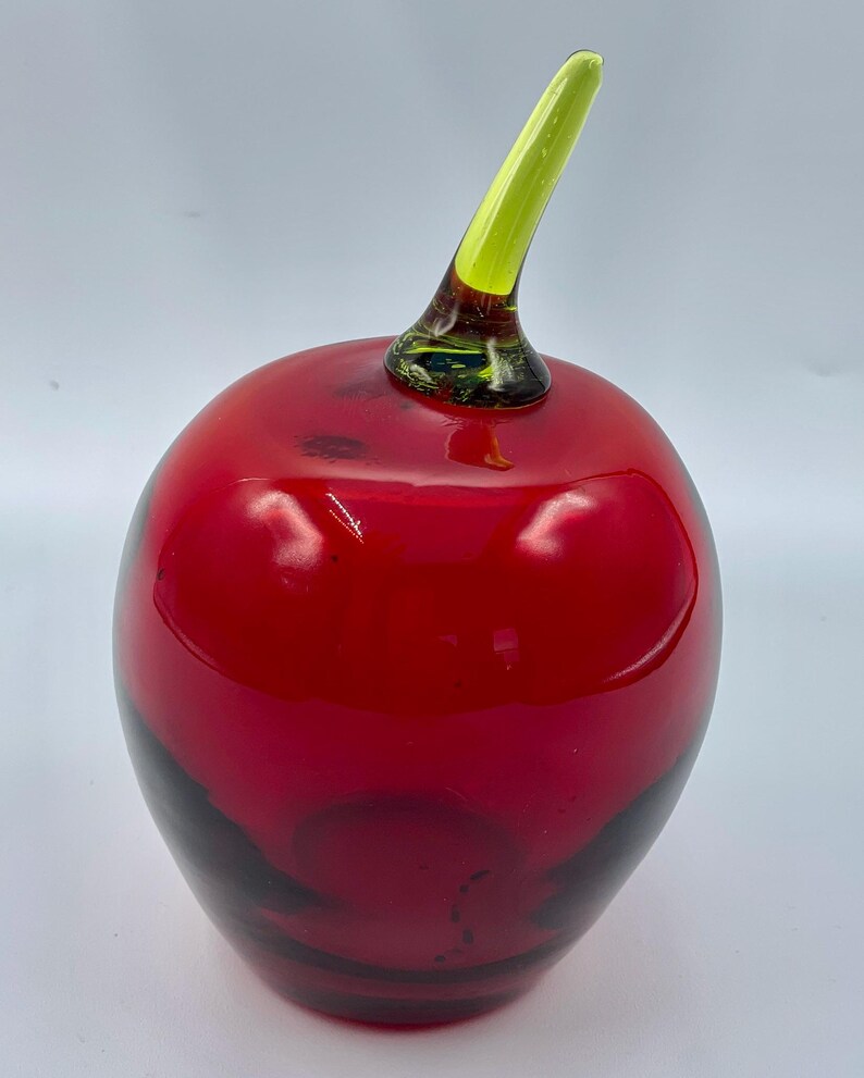 May include: A red glass apple with a green glass stem. The apple is a decorative object.