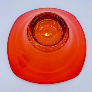 Pu&ograve; includere: Una ciotola di vetro arancione brillante con una forma arrotondata leggermente quadrata. La ciotola ha una sezione centrale rialzata che &egrave; leggermente pi&ugrave; scura.