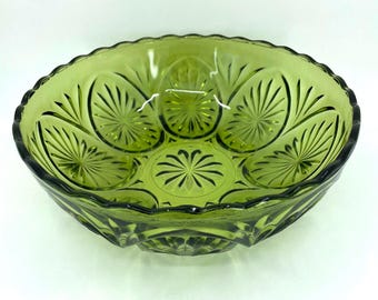 May include: A green glass bowl with an oval shape and a scalloped rim. The bowl features a detailed pattern of radiating lines and floral designs. The glass has a slight transparency, allowing light to pass through. This decorative bowl is suitable for serving or display.