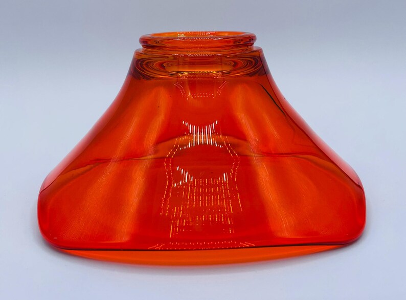 Pu&ograve; includere: Un vaso di vetro arancione brillante con una base larga e svasata e un'apertura stretta. Il vaso &egrave; in vetro trasparente con una leggera sfumatura arancione.