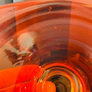 Pu&ograve; includere: Un primo piano di un vaso di vetro trasparente con una base rotonda di colore arancione. Il vaso ha un'apertura larga e un collo stretto. Il vaso &egrave; vuoto.