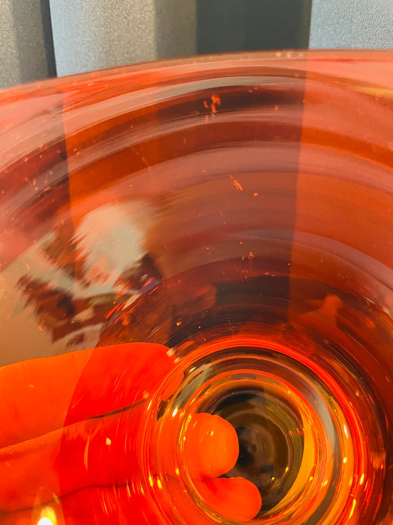Pu&ograve; includere: Un primo piano di un vaso di vetro trasparente con una base rotonda di colore arancione. Il vaso ha un'apertura larga e un collo stretto. Il vaso &egrave; vuoto.