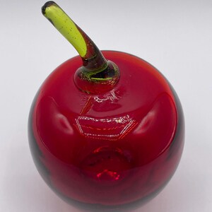 May include: A red glass apple with a green glass stem. The apple is a decorative object.