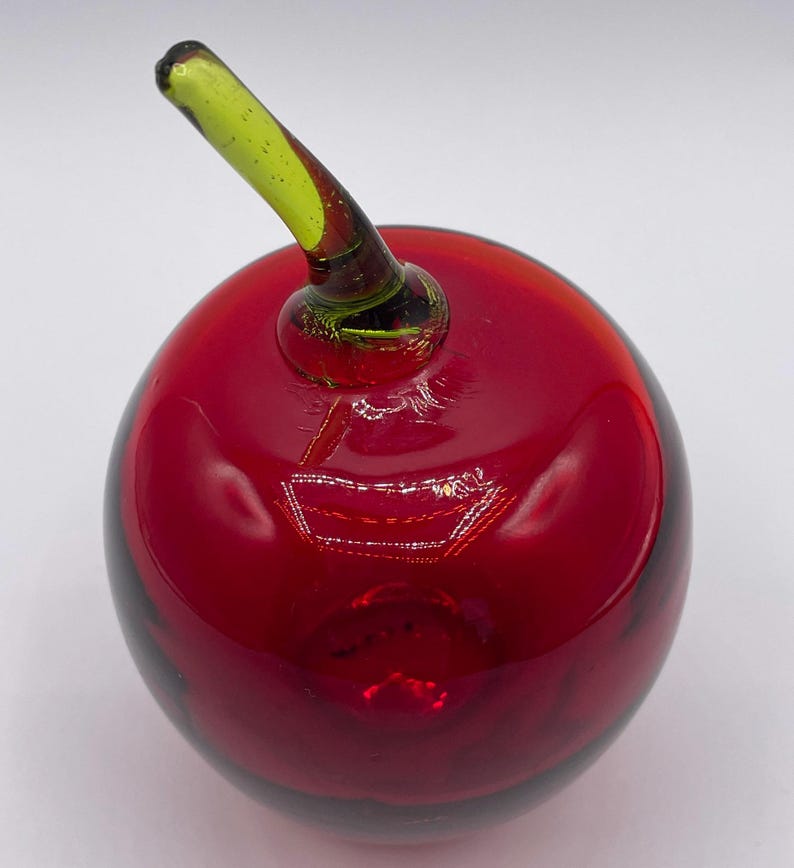 May include: A red glass apple with a green glass stem. The apple is a decorative object.