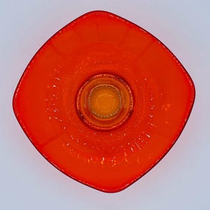 Pu&ograve; includere: Un piatto quadrato di vetro arancione con un piatto rotondo di vetro arancione pi&ugrave; piccolo al centro. Il piatto ha una superficie testurizzata.