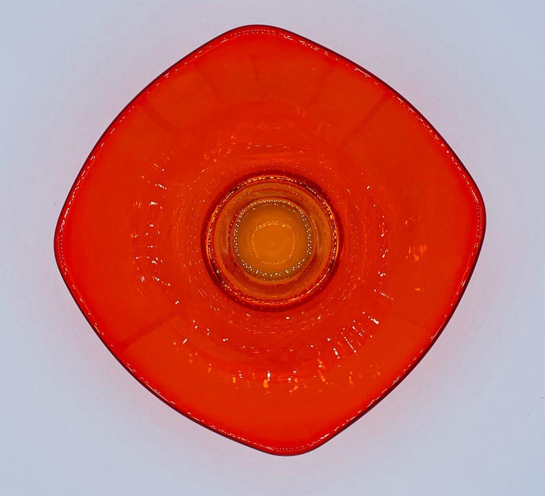 Pu&ograve; includere: Un piatto quadrato di vetro arancione con un piatto rotondo di vetro arancione pi&ugrave; piccolo al centro. Il piatto ha una superficie testurizzata.