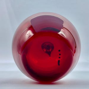 May include: A deep red glass vase with a round shape and a small, dark mark on the bottom.
