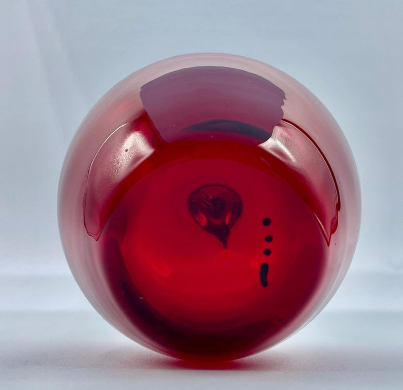 May include: A deep red glass vase with a round shape and a small, dark mark on the bottom.