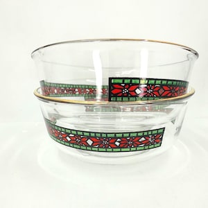 Könnte beinhalten: Zwei transparente Glasschalen übereinander gestapelt. Jede Schale hat einen goldenen Rand und ein dekoratives Band mit roten Weihnachtssternen, weißen geometrischen Formen und grünen Rändern. Die Schalen stehen auf einer weißen Oberfläche.