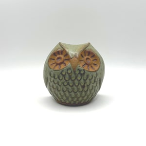 May include: A ceramic owl ornament in green and brown tones. The owl features large, circular eyes and a textured surface. This decorative figurine is suitable for home decoration.
