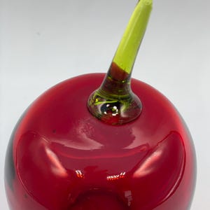 May include: A red glass apple with a green glass stem. The apple is a decorative object.