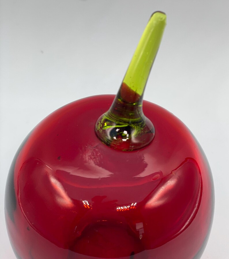 May include: A red glass apple with a green glass stem. The apple is a decorative object.