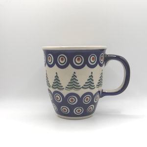 Könnte beinhalten: Eine Keramiktasse mit dunkelblauem und weißem Design. Die Tasse hat ein sich wiederholendes Muster aus blauen Kreisen mit braunen Zentren und grünen Weihnachtsbäumen. Der Griff und der Rand sind dunkelblau.