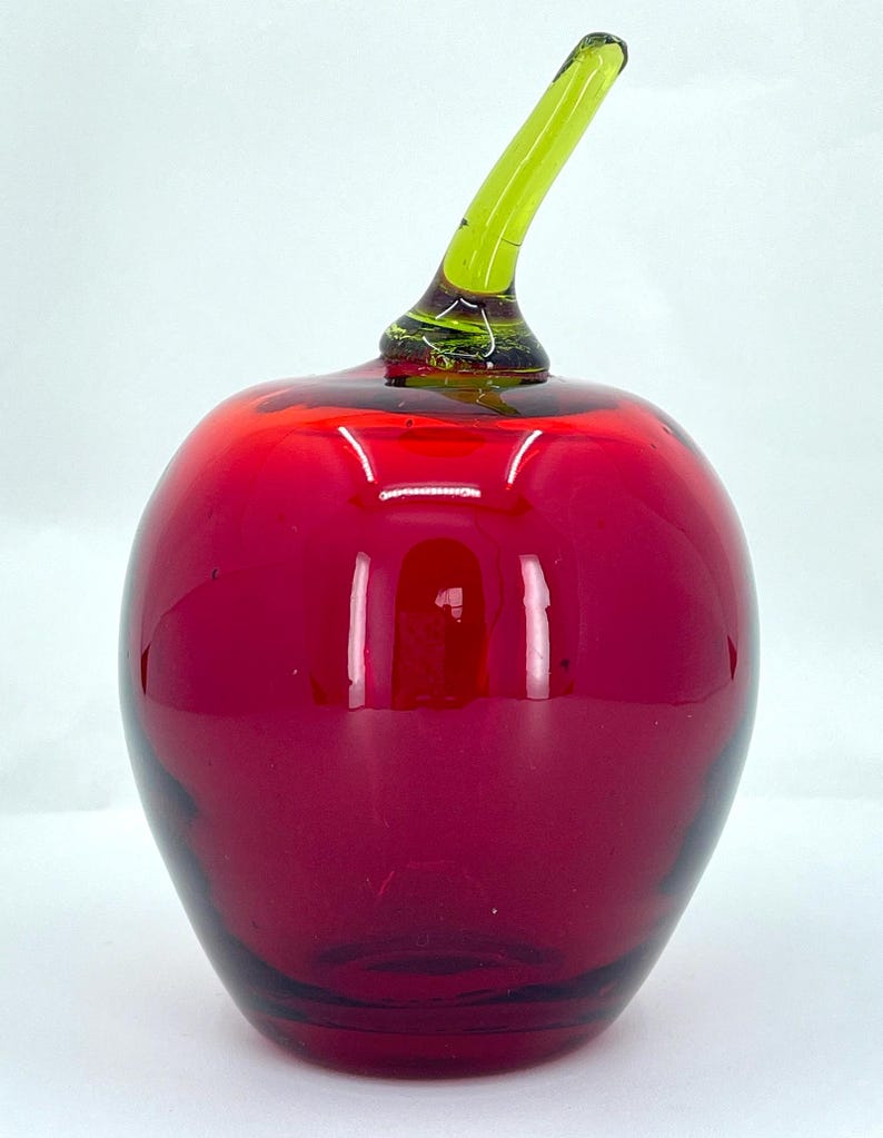 May include: A red glass apple with a green glass stem. The apple is a decorative object.