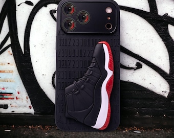 Funda para iPhone negra con diseño de zapatillas 3D, estilo streetwear moderno.
