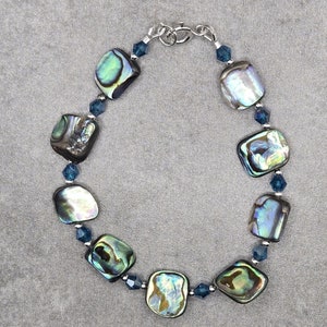 Puede incluir: Un brazalete de plata con cuentas de concha de abulón azul y verde iridiscente y cuentas de cristal azul oscuro.