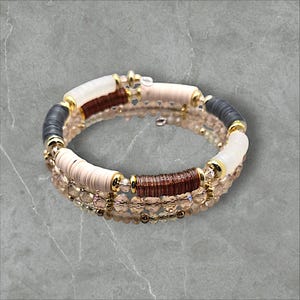 Peut inclure: Un bracelet multi-rangs composé de perles brunes, blanches et grises, avec des accents dorés et des perles de cristal transparentes.