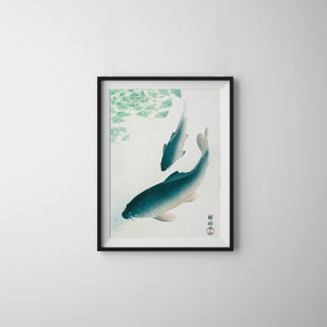 Puede incluir: Una impresión enmarcada de una pintura de estilo japonés que representa dos peces koi azules y blancos nadando en un estanque con hojas verdes. La impresión tiene un sello rojo con caracteres japoneses en la esquina inferior derecha.