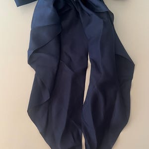 May include: A navy blue satin hair bow with long, flowing tails. The bow is secured with a silver-toned metal clip, and the word "HAND MADE" is visible on the clip. The bow is a stylish hair accessory.