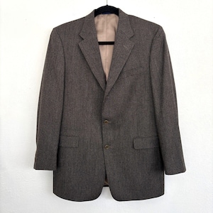 Op de afbeelding: Een bruine blazer met een sluiting met twee knopen, een revers met inkepingen en twee voorzakken. De blazer hangt aan een zwarte hanger tegen een witte achtergrond. De binnenvoering is lichtbruin.