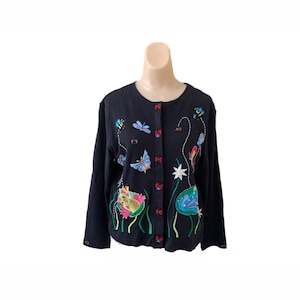 Könnte beinhalten: Ein schwarzer Cardigan mit Knöpfen und gestickten Schmetterlingen, Blumen und anderen naturinspirierten Designs.