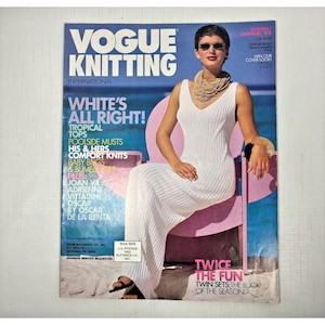 Może przedstawiać: Okładka magazynu Vogue Knitting International przedstawiająca kobietę w białej dzianinowej sukience siedzącą na różowym krześle. Tekst na okładce brzmi "White's All Right!" i "Twice the Fun Twin Sets the Look of the Season."