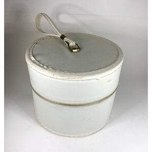 May include: White hat box with a white handle and a gold zipper. The box is round and has a white fabric exterior.