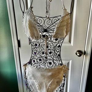 May include: White crochet bikini top and bottom with beaded accents. The bikini is displayed on a black wire mannequin.