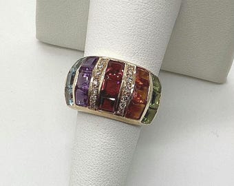 May include: A gold ring with a multi-colored gemstone band. The band features a row of square-shaped gemstones in shades of blue, purple, red, orange, and green, separated by a row of small, round diamonds.