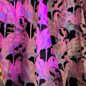 May include: A black button-up shirt with a pink and blue flamingo print. The shirt has a small embroidered patch of a cartoon character with multiple eyes.