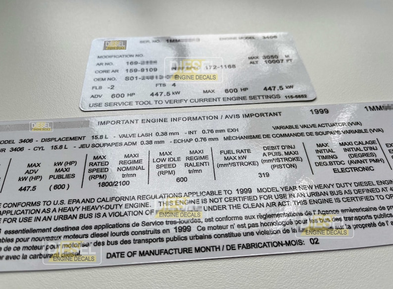 Op de afbeelding: Close-up van een wit label met zwarte tekst met details over de motorspecificaties voor een zware dieselmotor uit modeljaar 1999. Het label bevat informatie over de cilinderinhoud van de motor, de klepspeling, het brandstofverbruik en het maximale vermogen. De tekst "IMPORTANT ENGINE INFORMATION/AVIS IMPORTANT" staat bovenaan het label.