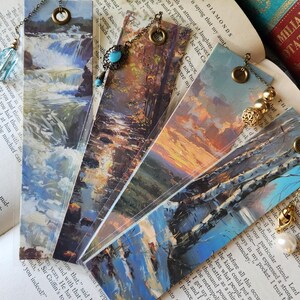 Puede incluir: Cinco marcapáginas vintage con imágenes coloridas de escenas de la naturaleza. Cada marcapáginas tiene una cadena y un amuleto decorativo. Los amuletos incluyen una cuenta de vidrio azul, una cuenta dorada, una perla y una cuenta dorada y azul.