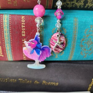 May include: Two blue velvet bookmarks with silver clasps and beaded chains. One bookmark features a pink and purple fish charm in a pink glass. The other bookmark features a pink and white seashell charm with a silver starfish.