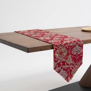 May include: A wooden table with a red and gold patterned table runner. The table has a unique angled leg design and a black square base. A white sphere sits on a small wooden tray on the table.
